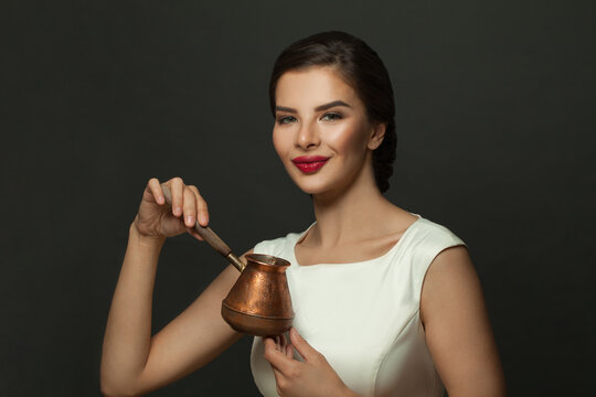 Beautiful young woman holding coffee ibric standing on black background