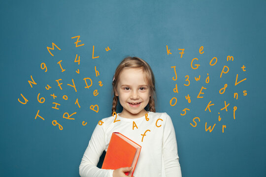 Happy smiling kid girl with book having fun against blue background with letters
