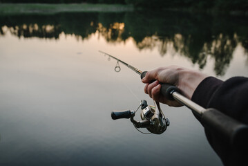 Man catching fish, pulling rod while fishing from lake or pond. Fisherman with rod, spinning reel...