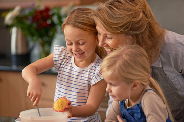 A joyful kitchen experience. Shot of two little girls baking cupcakes with their grandmother at home.