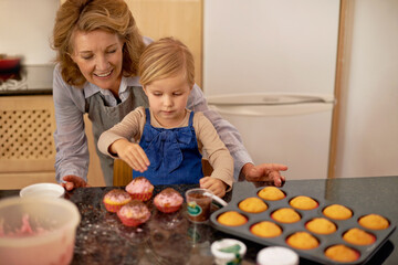 Obraz na płótnie Canvas Cake Boss at work. A little girl decorating cupcakes with the help of her grandmother.
