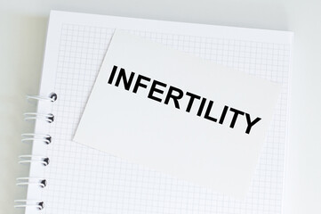 INFERTILITY text on a white card on the background of a notebook on the table