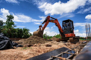 An orange mini excavator is digging sand at the construction site.