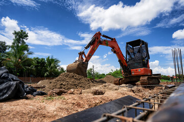 An orange mini excavator is digging sand at the construction site. © Phoophinyo