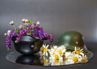 two models of military helmets black and khaki with bouquets of wildflowers and daisies