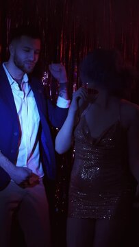 Party couple. New year night fun. Festive celebration. Happy amused man glamour woman enjoying dancing together in dark blue red neon flicker light smoke on tinsel vertical.