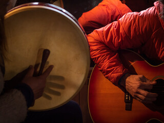 Female bodhrán player and male guitar player with an orange jacket.