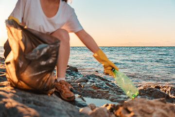 A female activist collects plastic bottles in a garbage bag. Close-up, out of focus. The sea is in...