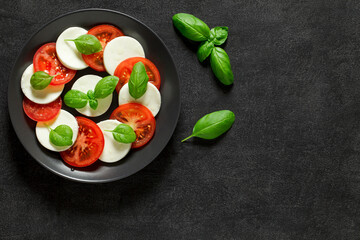 Caprese on plate and basil leaves, on dark background, top view, space to copy text.