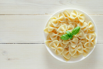 Farfalle, cooked pasta with basil green leaves, on plate, on white wooden board background, top view, space to copy text..