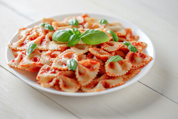 Farfalle pasta cooked with tomato sauce and basil, in a white plate, selective focus.