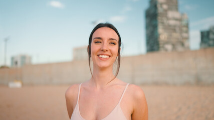 Portrait of young athletic woman with long ponytail wearing beige sports top on sandy city beath