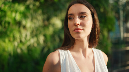 Naklejka premium Portrait of young woman with freckles and dark loose hair wearing white top and jeans looks at the camera