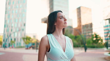 Lovely young woman with freckles and dark loose hair wearing white top and jeans is enjoying the view of modern city. Beautiful girl with long eyelashes looks at the upper floors of building