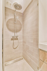 Shower faucets attached to tiled wall near glass partition and ornamental curtail in washroom at...