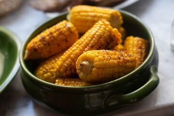 Grilled sweet corn cobs in a green ceramic bowl