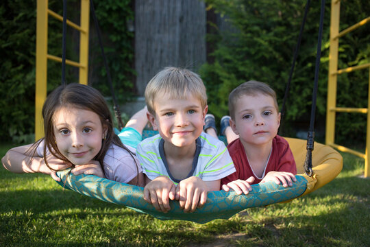 three children, a girl and boys, brothers and sister, swing lying on a swing in the playground. Cheerful childhood, carelessness, summer holidays, joy, enjoy the moment. Selective focus
