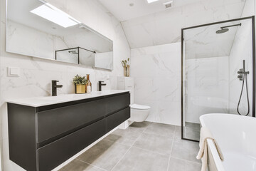 The interior of a modern toilet with a bath and shower, sinks, black furniture and a large...