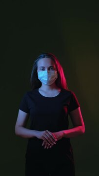 Hygiene protection. Coronavirus prevention. Woman in medicine mask blue red neon light glow looking at camera isolated on black vertical. Stay safe. New normal. Quarantine measures