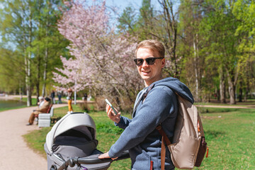 A young man father walks with a stroller with a child in a summer park