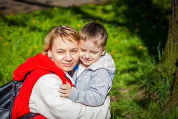 Children with their mother pose in a sunny clearing near a tree in the forest. The sun's rays envelop the space. Interaction history. Space for copying.