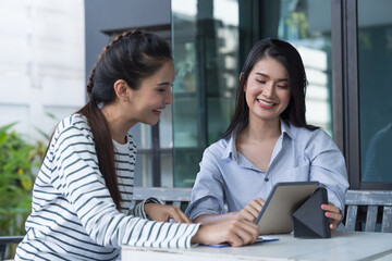 Two Asian young women using digital tablet at the outdoor office. Group of happy asian women colleagues working with tablet outdoor office.