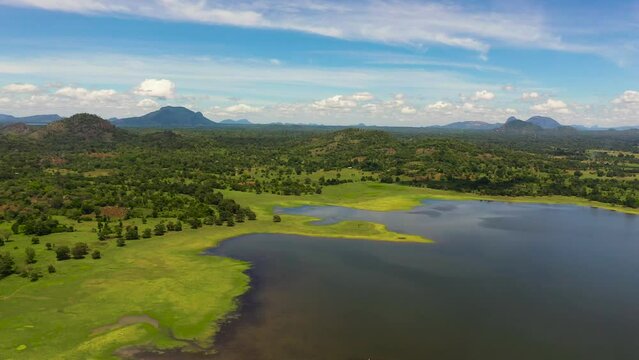 A valley with a lake and tropical vegetation against a blue sky and clouds. Sorabora lake, Sri Lanka.