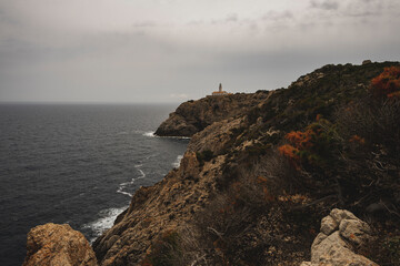Biała latarnia morska na skalistym klifie w pochmurny dzień. Latarnia położona jest na wschodnim wybrzeżu Majorki.  - obrazy, fototapety, plakaty
