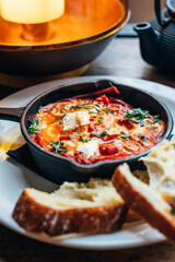 Freshly made shakshuka with spiced tomato, red pepper, feta, egg, coriander and pieces of homemade sourdough, served in iron pan, healthy vegetarian breakfast