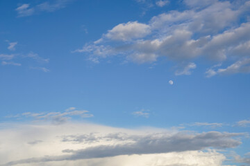Background with white clouds and moon in the blue sky in the early evening