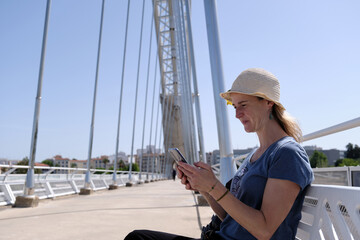 Cheerful woman using smartphone on bridge