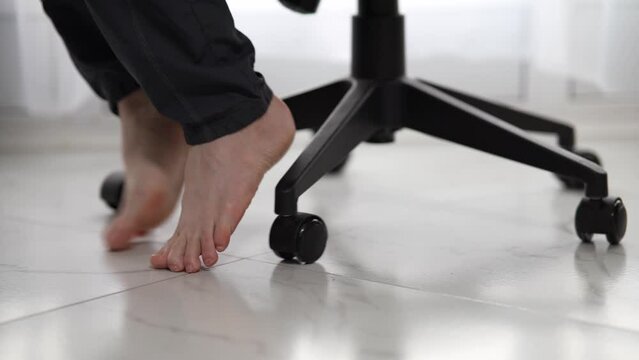 Barefoot men's feet on an office chair with wheels on white porcelain stoneware