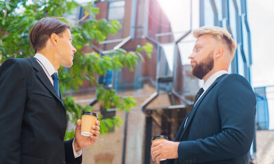 Confident businessman and his colleague in front of modern office building. Financial investors in...