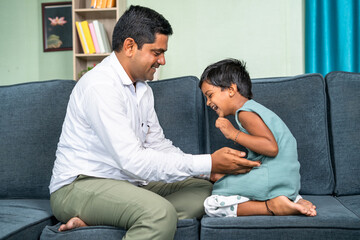 Father cuddling his little daughter after coming from office at home while sitting on sofa -...