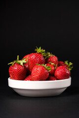 Red fresh strawberries in a white plate on a black background. Summer seasonal berries, close-up