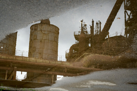 Spiegelbild einer alten verlassenen Industriekulisse eines alten Stahlwerks in einer Regenpfütze auf einem grauen Boden