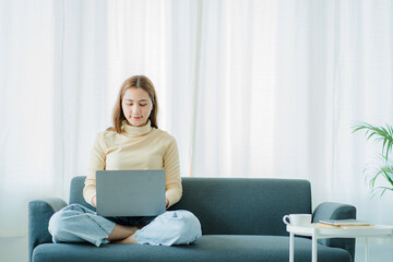 A freelance Asian woman working on a laptop checks social media while sitting on the sofa relaxing in her living room at home. concept of lifestyle for women