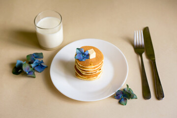 Foodphoto. On a beige background - pancakes on a paper backing. Decorated with oil, blue hydrangea flowers, green spikelets. Nice breakfast and lunch. Daylight. Illustration for a recipe.