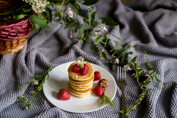 Foodphoto. Pancakes with strawberries close-up. decorated with flowers. The composition is complemented by leaves and greens in a basket. Picnic or summer breakfast.