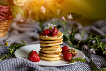 Foodphoto. Pancakes with strawberries close-up. decorated with flowers. The composition is complemented by leaves and greens in a basket. Picnic or summer breakfast.
