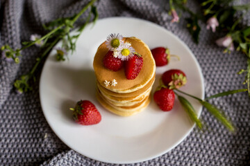 Foodphoto. Pancakes with strawberries close-up. decorated with flowers. The composition is complemented by leaves and greens in a basket. Picnic or summer breakfast.