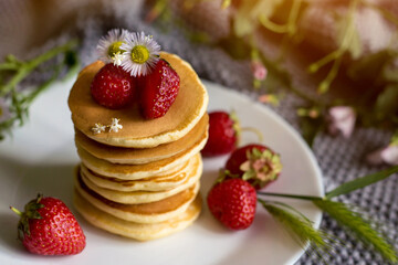 Foodphoto. Pancakes with strawberries close-up. decorated with flowers. The composition is complemented by leaves and greens in a basket. Picnic or summer breakfast.