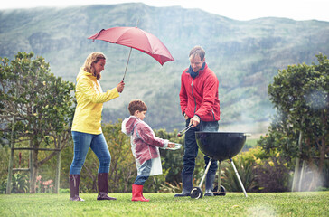 They didnt let a little rain spoil their barbecue. Shot of a family having a barbecue outside in...