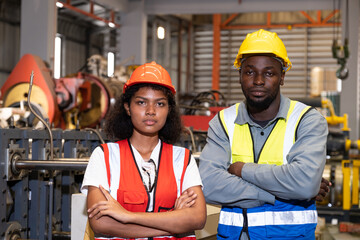 African mechanical engineer team, wearing safety equipment. While doing machine maintenance and safety control while work inside of factory area. With blurred background of heavy machine.