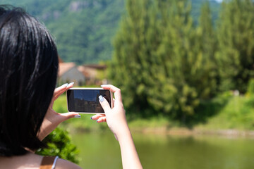 Young Asian women using smartphone to take photo of travel location. Summer vacation concept with nature and using technology for live stream influencer or social network review concept.