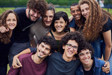Life is brighter with friends. Portrait of a group of young students standing arms around each other outside in a park during the day.