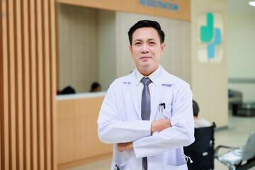 Asian male doctor in white uniform look at camera standing in patient reception at modern hospital....