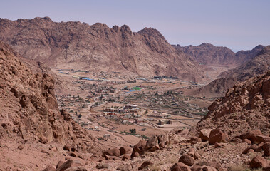 Saint Catherine, Egypt - panoramic view of the city downtown from Abu Jeefa pass on the sunny morning. The city is UNESCO world heritage site. Red mountains at the background.