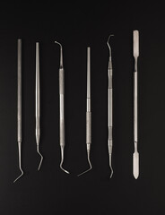 Set of dental metal instruments for treating and checking teeth. Top view on black background
