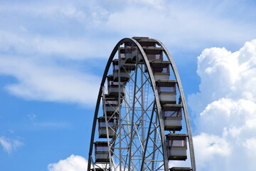 giant ferris wheel detail. white gondolas. steel frame construction. giant spokes in large wheel. leisure and relaxation concept. parks and outdoors. blue sky amd white clouds. entertainment and fun.